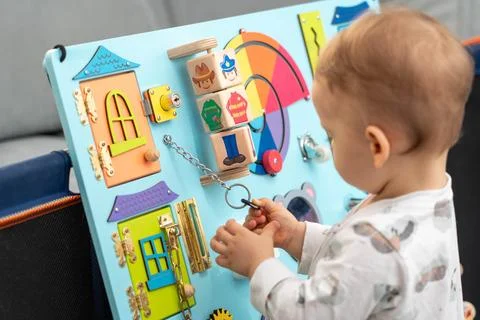 Baby pulls a key on a chain while playing with a busy board Stock Photos