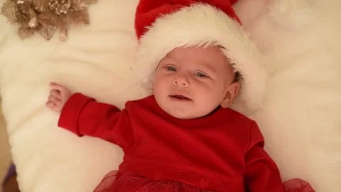 Baby in red Santa hat and red dress lies on white blanket. Stock Footage 219244397