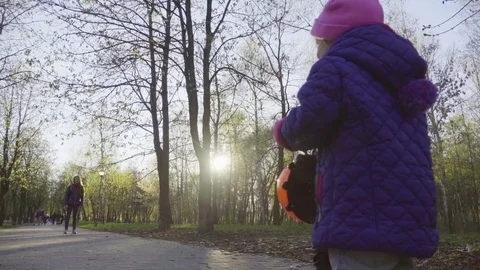 Baby is riding a scooter along the park path towards her mom, slow motion Stock Footage