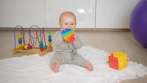 The baby sits on the floor and chews on a pop it or simple dimple. Various t Stock Footage