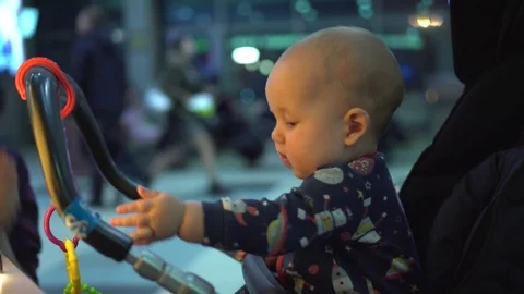 Baby sits in a stroller and playing with colorful toy plastic chain Stock Footage 80286476