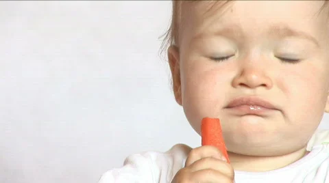 Baby sits at a table and eats a carrot Stock Footage