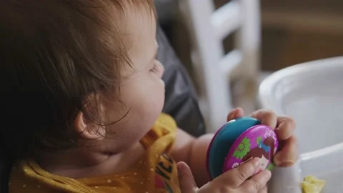 Baby sitting at the baby's table playing with a toy while being fed by his Stock Footage 170468879