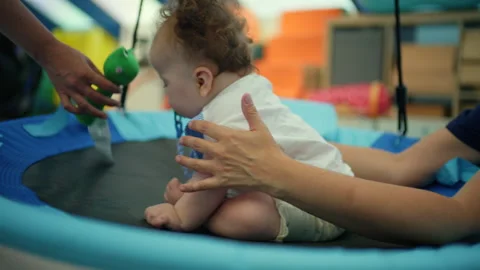 Baby sitting on a blue swing, learning and playing during a physical therapy Video stock 342873651