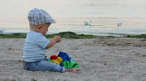 Baby sitting down and playing with his hands on the beach Video stock 12274836