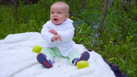 The baby sitting on the grass and eats the big Apple Видео 76471689