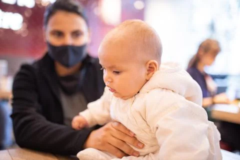 Baby sitting on a restaurant table while her mother holds her by her leg Stock Photos