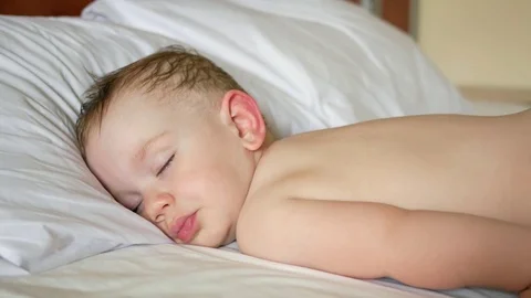 Baby is sleeping on a white bed without a shirt. A little sweating hair. Close Video stock 76367006