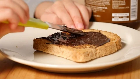 Baby is spreading chocolate on slice of bread. greedy food, healthy greedy food. Stock Footage 100303663