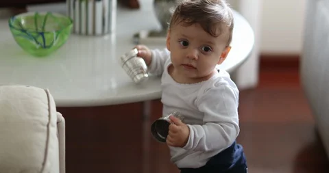 Baby standing up at home holding objects and falling down on floor Video stock 129051331