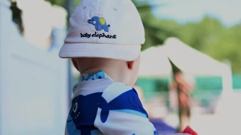 Baby in a sun hat eats watermelon outdoors and turns to look around in the Stock Footage 347686483