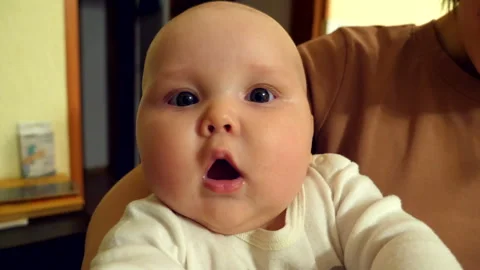 Baby with a surprised expression looking directly at the camera in home Video stock 302236252