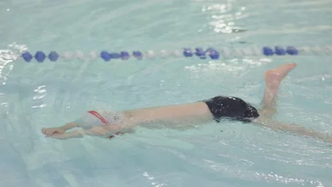 Baby swimmer learning to swim using only legs in blue transparent swimming pool Stock Footage 203602641