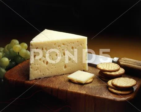 Baby Swiss Cheese Wedge On A Cutting Board With Crackers And Green Grapes
