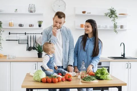 Baby on table staring at parents while dad chewing cucumber 스톡 사진