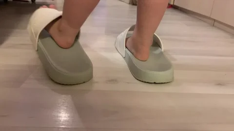 Baby takes his first steps. Baby walks with her little feet in big adult flip Stock Footage 263327914