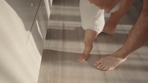 Baby taking first steps. The father holds and supports the child and teaches him Vídeos de archivo 159403993
