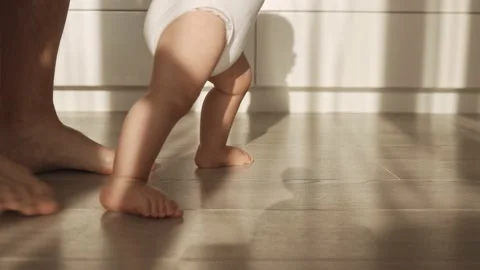 Baby taking first steps. The father holds and supports the child and teaches him Stock Footage 159404152