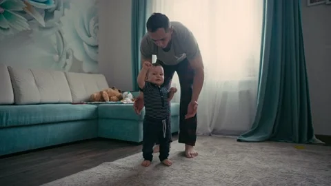 Baby taking first steps with father's help at home. Father Encouraging Baby Son Видео 165307395