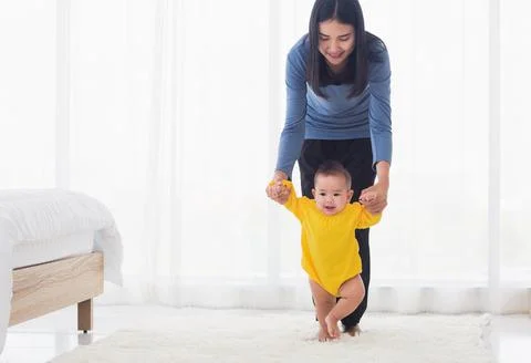 Baby taking first steps learning to walk with mother Stock Photos