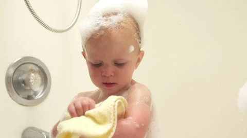 A baby washes himself with a washcloth while taking a bubble bath Vídeo Stock 33871531