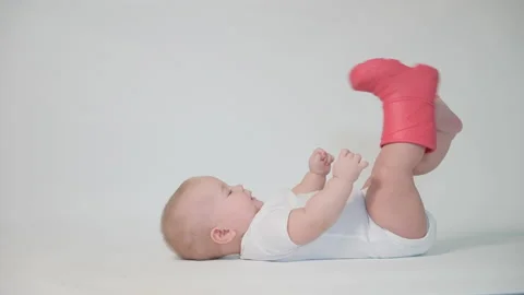 The baby on the white background is lying on his back with one boot trying to 스톡 동영상 237240516
