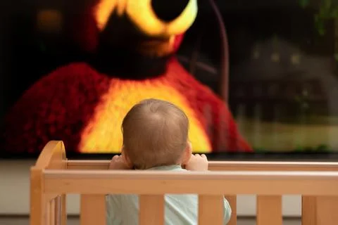 The baby's cute head is barely visible from the crib. Watching cartoons on TV Stock-Fotos