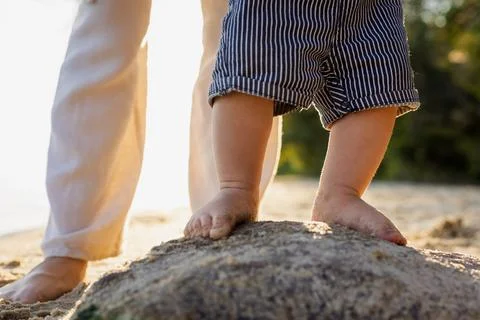 Baby's first steps on a rock at the beach during golden hour Stock Photos