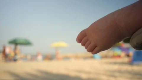 Baby's small foot with out of focus background of sunny beach and people Vídeos de archivo 343556792