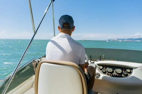 Bach view of middle-aged man driving luxury motor yacht. Captain at the helm of Stock-Fotos