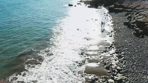 Back aerial view of young couple running on the black beach in Gran Canaria Stock Footage 95399031