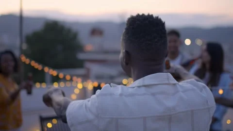 Back of African boy dancing lively at rooftop evening gathering with group of Stock Footage 263510017