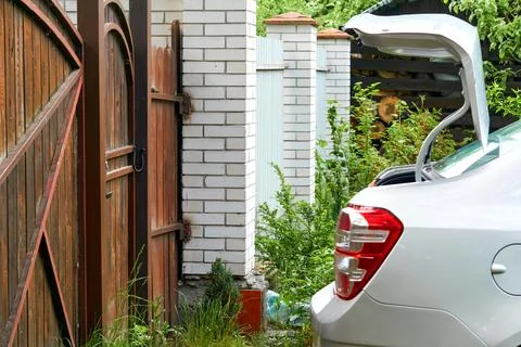 Back of the car with headlights and an open trunk. Brick fence. wooden gates Stock Photos