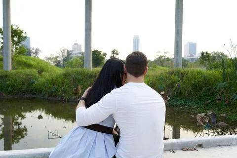 Back of a couple embraced while looking to the sunset in an urban park Stock Photos