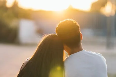 Back of a couple facing the sunset while embracing outdoors Stock Photos