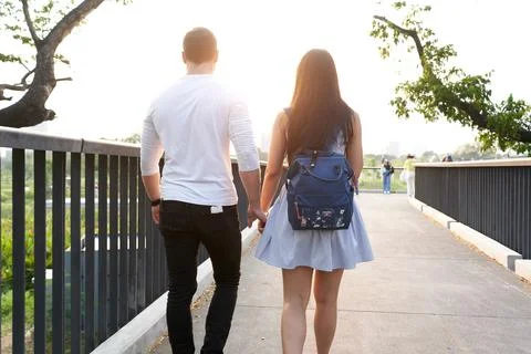 Back of couple walking throug a bridge holding hands during sunset Stock Photos