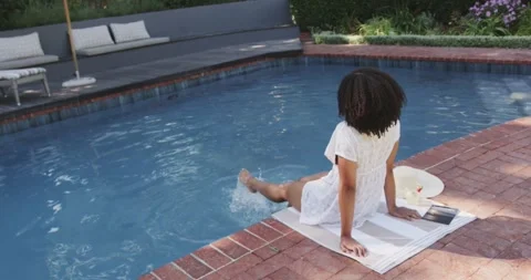 Back-facing figure is lowering legs into pool at brick coping, then is kicking Stock Footage 337294512