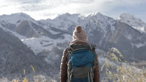 The back of a girl in a winter jacket and hat with a large backpack looks into Stock Footage 218319084