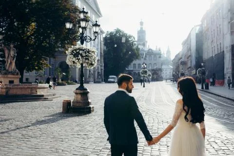 Back half-length view of the gorgeous happy newlywed couple holding hands in the Stock Photos