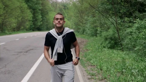 Back look of a young man in hood running on the road near the forest 4K Stock Footage 75543543