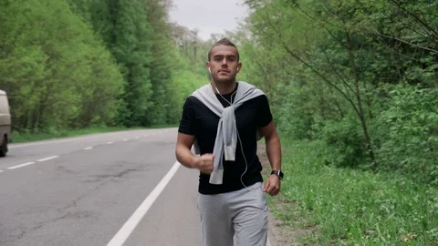 Back look of a young man in hood running on the road near the forest 4K Stock Footage 75543735
