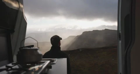 Back of man by camper van kitchen enjoy Jotunheimen sunset rainstorm view Stock Footage 253774256