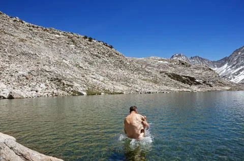 Back Of Man Jumping Into Alpine Lake Stock Photos