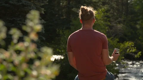 Back of Man Sitting On Rock in Nature with Glass of Wine by Outdoor Stream Video stock 125638522