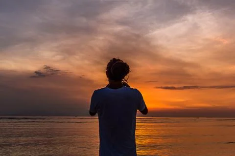 The back of a man standing on a beach, taking a photo in the sunset Stock Photos