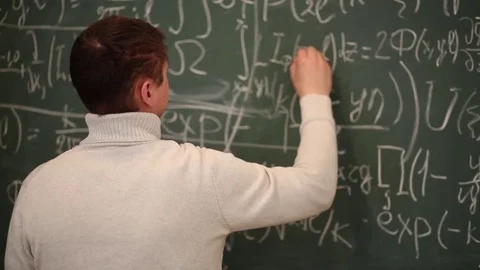 Back of man in sweater correcting symbols in equations on blackboard. Video stock 69988259