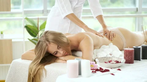 Back massage on massage table with flowers and candles to beautiful blonde girl Video stock 137574268