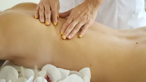 Back massage on massage table with flowers and candles to beautiful blonde girl Stock Footage 137653105