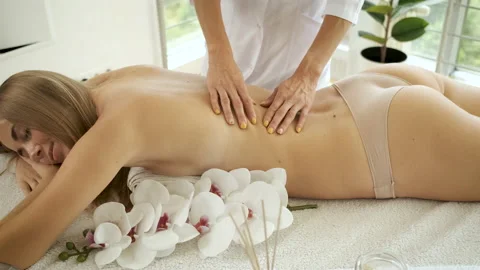 Back massage on massage table with flowers and candles to beautiful blonde girl Stock Footage 139044805