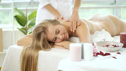 Back massage on massage table with flowers and candles to beautiful blonde girl Stock Footage 139837327